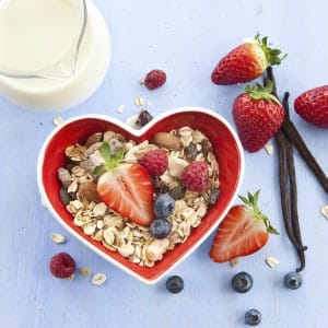 Muesli in heart-shaped bowl with fresh berries and milk