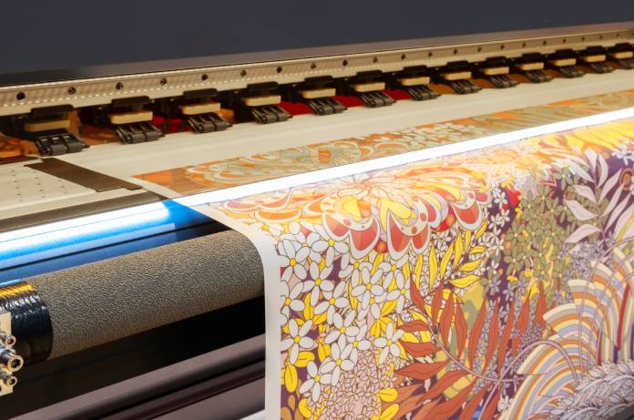Image of a wide-format printer turning out a large and colorful print of a drawing of flowers and leaves.