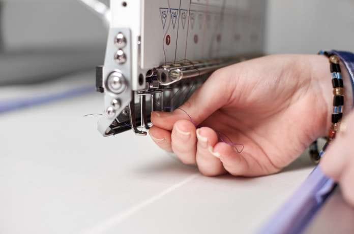 A close-up of a woman's hand wearing a beaded bracelet, filling purple thread into an embroidery machine.