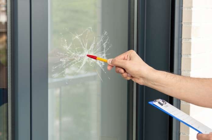 A person holding a clipboard and pushing the tip of a capped pen against an impact crack in a large window.