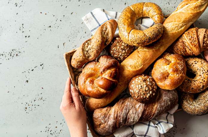 Someone placing a tray of artisan baked goods onto the counter. There are bagels, baguettes, and more.