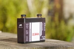 Home 20 A lithium-ion motorcycle battery sitting on a picnic table. Behind it is a blurred background of trees.