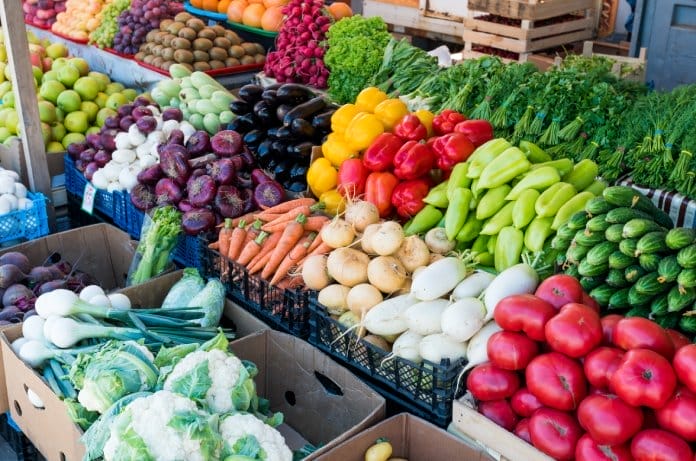 A selection of locally farmed and sourced produce at a farmers' market, including tomatoes, carrots, peppers, and more.