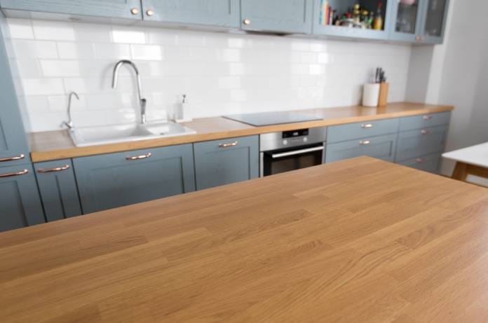 A modern kitchen contains wooden countertops, blue cabinets with copper pulls, a white sink, a black cooktop, and an oven.