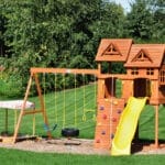 Home 13 A home swing set in the backyard with a yellow slide and a wooden frame. There's mulch underneath the set.