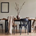 A well-lit dining room with a wooden table. The table is set and there are four chairs around it, two black and two brown.