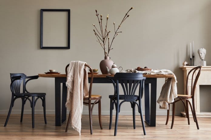 A well-lit dining room with a wooden table. The table is set and there are four chairs around it, two black and two brown.