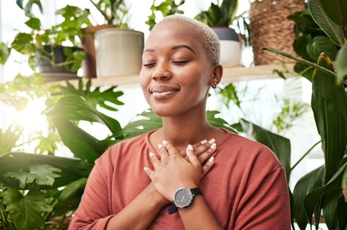 A Black woman with blonde hair is practicing balance, breathing plants for zen meditation in a greenery nursery.
