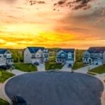 A beautiful neighborhood of modern, well-groomed homes and yard in a cul de sac. The sun is setting in the background.
