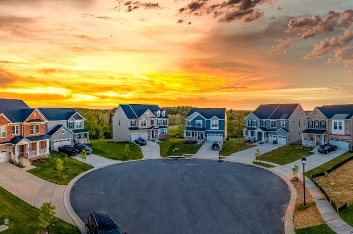 A beautiful neighborhood of modern, well-groomed homes and yard in a cul de sac. The sun is setting in the background.