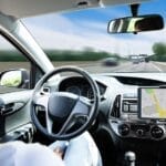 A female driver behind the wheel of an autonomous vehicle. There's a blurred view out the front windshield.