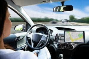 A female driver behind the wheel of an autonomous vehicle. There's a blurred view out the front windshield.