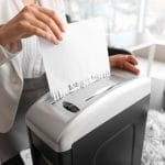 A young professional woman in business attire is shredding a large amount of important work documents in her office.