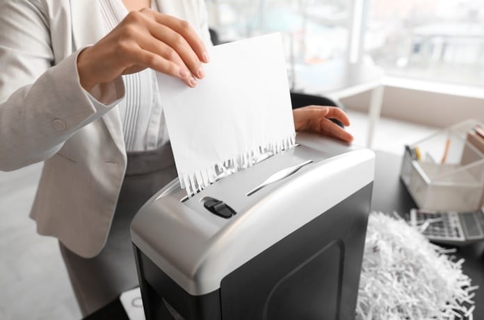 A young professional woman in business attire is shredding a large amount of important work documents in her office.