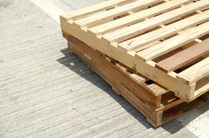 Three wooden pallets are stacked on top of each other, sitting on a concrete surface during a sunny day.