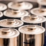 An extreme close-up of multiple silver AAA batteries, showing only the top halves and the positive charge signs.