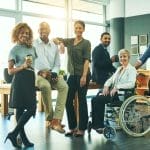 A group of men and women of different ethnicities, including a woman in a wheelchair, inside a conference room.