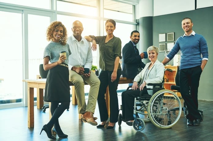 A group of men and women of different ethnicities, including a woman in a wheelchair, inside a conference room.